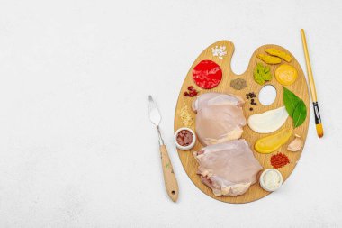 Çiğ tavuk butları, renkli baharatlar ve ahşap bir palette sos ile yaratıcı mutfak konsepti. Aşçıyı gurme mutfağında temsil eden yemek sanatı fikri.