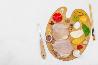 Çiğ tavuk butları, renkli baharatlar ve ahşap bir palette sos ile yaratıcı mutfak konsepti. Aşçıyı gurme mutfağında temsil eden yemek sanatı fikri.