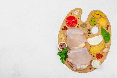 Çiğ tavuk butları, renkli baharatlar ve ahşap bir palette sos ile yaratıcı mutfak konsepti. Aşçıyı gurme mutfağında temsil eden yemek sanatı fikri.