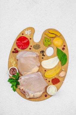 Çiğ tavuk butları, renkli baharatlar ve ahşap bir palette sos ile yaratıcı mutfak konsepti. Aşçıyı gurme mutfağında temsil eden yemek sanatı fikri.