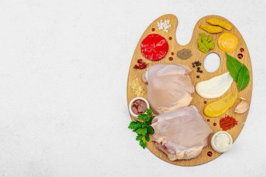 Çiğ tavuk butları, renkli baharatlar ve ahşap bir palette sos ile yaratıcı mutfak konsepti. Aşçıyı gurme mutfağında temsil eden yemek sanatı fikri.