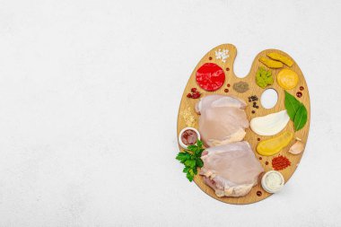 Çiğ tavuk butları, renkli baharatlar ve ahşap bir palette sos ile yaratıcı mutfak konsepti. Aşçıyı gurme mutfağında temsil eden yemek sanatı fikri.