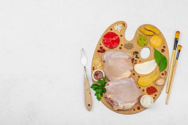 Çiğ tavuk butları, renkli baharatlar ve ahşap bir palette sos ile yaratıcı mutfak konsepti. Aşçıyı gurme mutfağında temsil eden yemek sanatı fikri.