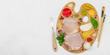 Çiğ tavuk butları, renkli baharatlar ve ahşap bir palette sos ile yaratıcı mutfak konsepti. Aşçıyı gurme mutfağında, afiş formatında temsil eden yemek sanatı fikri