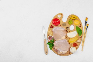 Çiğ tavuk butları, renkli baharatlar ve ahşap bir palette sos ile yaratıcı mutfak konsepti. Aşçıyı gurme mutfağında temsil eden yemek sanatı fikri.