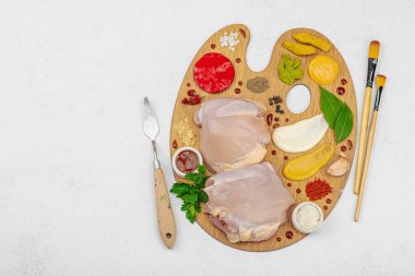 Çiğ tavuk butları, renkli baharatlar ve ahşap bir palette sos ile yaratıcı mutfak konsepti. Aşçıyı gurme mutfağında temsil eden yemek sanatı fikri.