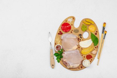 Çiğ tavuk butları, renkli baharatlar ve ahşap bir palette sos ile yaratıcı mutfak konsepti. Aşçıyı gurme mutfağında temsil eden yemek sanatı fikri.