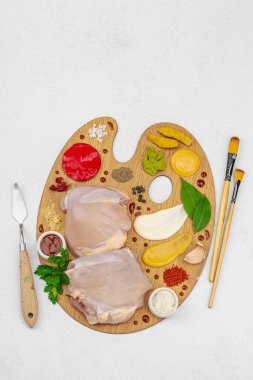 Çiğ tavuk butları, renkli baharatlar ve ahşap bir palette sos ile yaratıcı mutfak konsepti. Aşçıyı gurme mutfağında temsil eden yemek sanatı fikri.