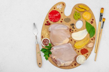 Çiğ tavuk butları, renkli baharatlar ve ahşap bir palette sos ile yaratıcı mutfak konsepti. Aşçıyı gurme mutfağında temsil eden yemek sanatı fikri.