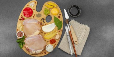 Çiğ tavuk butları, renkli baharatlar ve ahşap bir palette sos ile yaratıcı mutfak konsepti. Aşçıyı gurme mutfağında, afiş formatında temsil eden yemek sanatı fikri