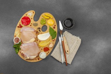 Çiğ tavuk butları, renkli baharatlar ve ahşap bir palette sos ile yaratıcı mutfak konsepti. Aşçıyı gurme mutfağında temsil eden yemek sanatı fikri.