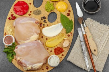 Çiğ tavuk butları, renkli baharatlar ve ahşap bir palette sos ile yaratıcı mutfak konsepti. Aşçıyı gurme mutfağında temsil eden yemek sanatı fikri.