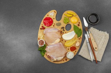 Çiğ tavuk butları, renkli baharatlar ve ahşap bir palette sos ile yaratıcı mutfak konsepti. Aşçıyı gurme mutfağında temsil eden yemek sanatı fikri.