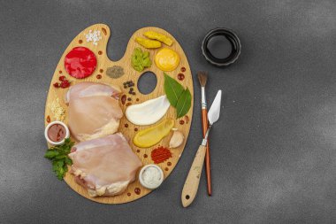 Çiğ tavuk butları, renkli baharatlar ve ahşap bir palette sos ile yaratıcı mutfak konsepti. Aşçıyı gurme mutfağında temsil eden yemek sanatı fikri.