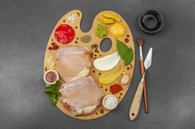 Çiğ tavuk butları, renkli baharatlar ve ahşap bir palette sos ile yaratıcı mutfak konsepti. Aşçıyı gurme mutfağında temsil eden yemek sanatı fikri.