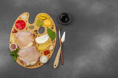 Çiğ tavuk butları, renkli baharatlar ve ahşap bir palette sos ile yaratıcı mutfak konsepti. Aşçıyı gurme mutfağında temsil eden yemek sanatı fikri.