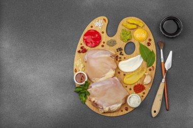 Çiğ tavuk butları, renkli baharatlar ve ahşap bir palette sos ile yaratıcı mutfak konsepti. Aşçıyı gurme mutfağında temsil eden yemek sanatı fikri.