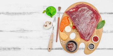 Çiğ biftek, çeşitli baharatlar, soslar ve ahşap bir ressamın paletinde yaratıcı bir şekilde sıralanmış otlarla dolu gurme yemek konsepti. Aşçılık ve aşçılık yaratıcılığı, beyaz ahşap arka plan, afiş