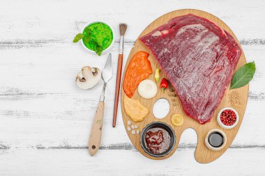 Çiğ biftek, çeşitli baharatlar, soslar ve ahşap ressamın paletinde yaratıcılıkla sıralanmış otlar içeren gurme yemek konsepti. Aşçılık ve aşçılık yaratıcılığı, beyaz ahşap arka plan, üst görünüm