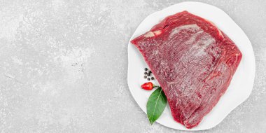 Beyaz seramik tabakta çeşitli baharatlarla taze çiğ biftek. Işık taşı arka planı. Et hazırlama, gurme pişirme veya yemek stili, afiş formatı için mutfak konsepti