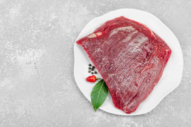 Beyaz seramik tabakta çeşitli baharatlarla taze çiğ biftek. Işık taşı arka planı. Et hazırlama, gurme pişirme ya da yemek tasarımı için mutfak konsepti.