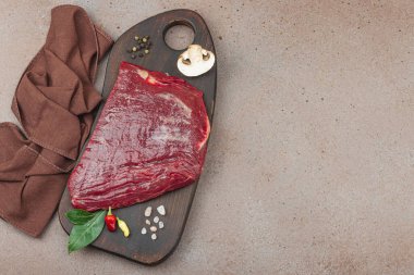 Tahta kesme tahtasının üzerinde çeşitli baharatlarla taze çiğ biftek. Et hazırlama, gurme pişirme ya da yemek tasarımı için mutfak konsepti.