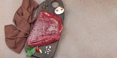 Tahta kesme tahtasının üzerinde çeşitli baharatlarla taze çiğ biftek. Et hazırlama, gurme pişirme veya yemek stili, afiş formatı için mutfak konsepti