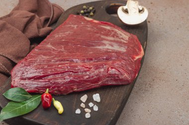 Tahta kesme tahtasının üzerinde çeşitli baharatlarla taze çiğ biftek. Et hazırlama, gurme pişirme veya yemek tasarımı için mutfak konsepti, kopyalama alanı