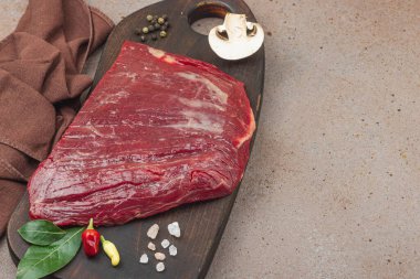 Tahta kesme tahtasının üzerinde çeşitli baharatlarla taze çiğ biftek. Et hazırlama, gurme pişirme veya yemek tasarımı için mutfak konsepti, kopyalama alanı