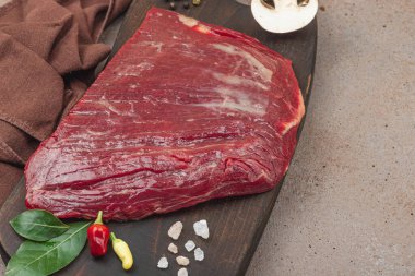 Tahta kesme tahtasının üzerinde çeşitli baharatlarla taze çiğ biftek. Et hazırlama, gurme pişirme veya yemek tasarımı için mutfak konsepti, kopyalama alanı