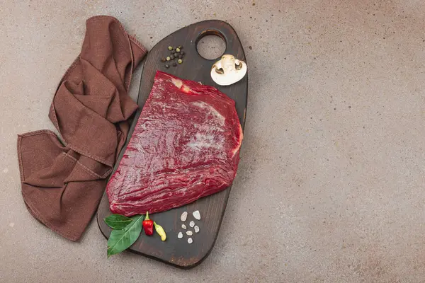 Tahta kesme tahtasının üzerinde çeşitli baharatlarla taze çiğ biftek. Et hazırlama, gurme pişirme ya da yemek tasarımı için mutfak konsepti.