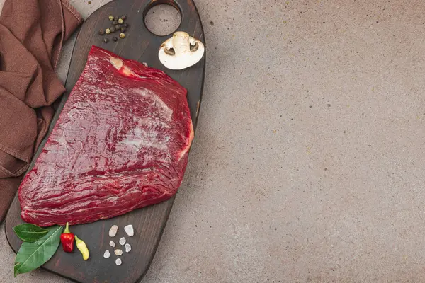 Tahta kesme tahtasının üzerinde çeşitli baharatlarla taze çiğ biftek. Et hazırlama, gurme pişirme ya da yemek tasarımı için mutfak konsepti.