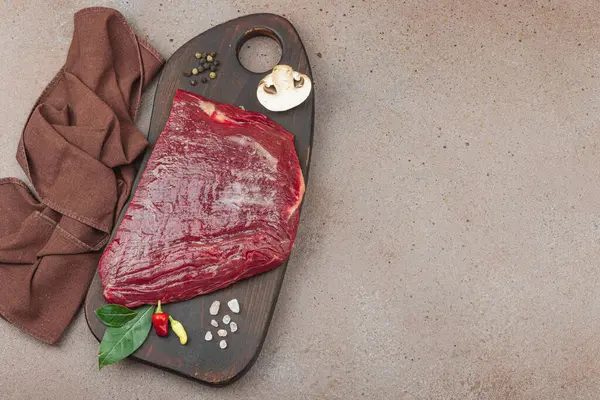 Tahta kesme tahtasının üzerinde çeşitli baharatlarla taze çiğ biftek. Et hazırlama, gurme pişirme ya da yemek tasarımı için mutfak konsepti.