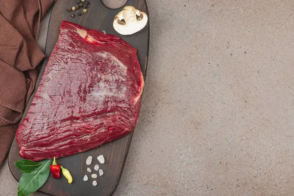 Tahta kesme tahtasının üzerinde çeşitli baharatlarla taze çiğ biftek. Et hazırlama, gurme pişirme ya da yemek tasarımı için mutfak konsepti.