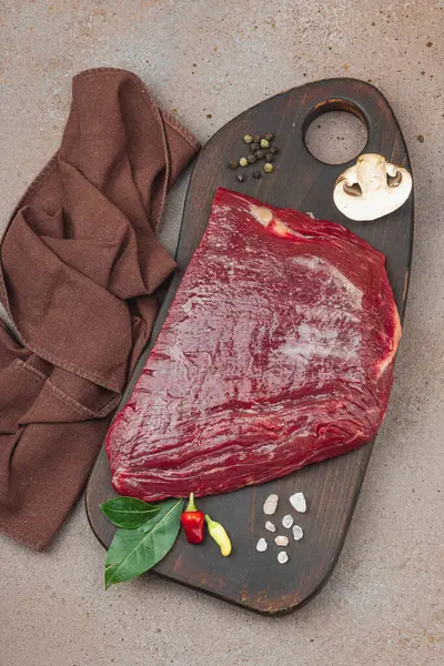 Tahta kesme tahtasının üzerinde çeşitli baharatlarla taze çiğ biftek. Et hazırlama, gurme pişirme ya da yemek tasarımı için mutfak konsepti.