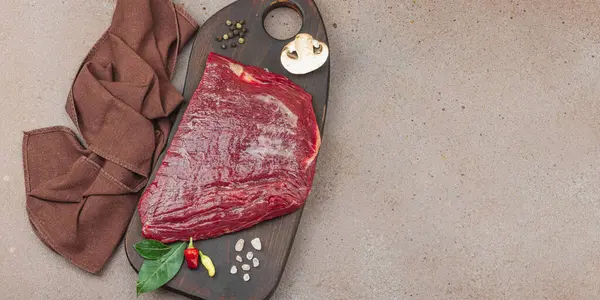 Tahta kesme tahtasının üzerinde çeşitli baharatlarla taze çiğ biftek. Et hazırlama, gurme pişirme veya yemek stili, afiş formatı için mutfak konsepti