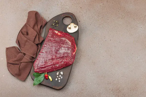 Tahta kesme tahtasının üzerinde çeşitli baharatlarla taze çiğ biftek. Et hazırlama, gurme pişirme ya da yemek tasarımı için mutfak konsepti.