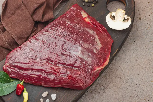 Tahta kesme tahtasının üzerinde çeşitli baharatlarla taze çiğ biftek. Et hazırlama, gurme pişirme ya da yemek tasarımı için mutfak konsepti.
