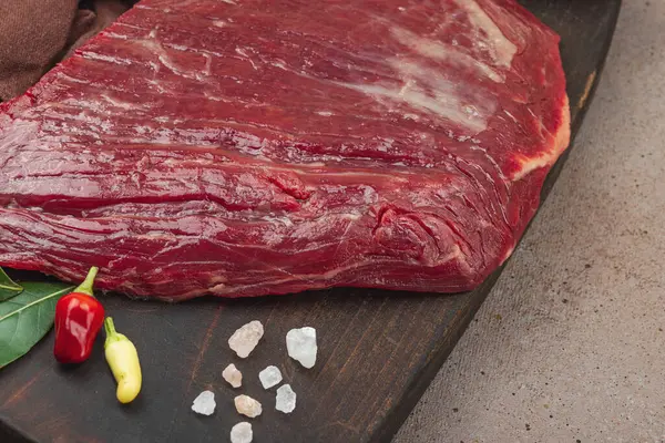 Tahta kesme tahtasının üzerinde çeşitli baharatlarla taze çiğ biftek. Et hazırlama, gurme pişirme ya da yemek tasarımı için mutfak konsepti.
