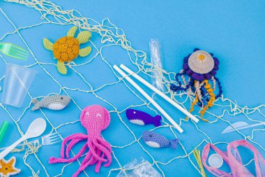 Dünya Okyanus Günü, su kirliliği farkındalığı ve çevresel eğitim görselleri. El yapımı tığ işi deniz hayvanları tek kullanımlık plastik eşyalar ve ağ, mavi arka plan, deri döşeme, üst görünüm
