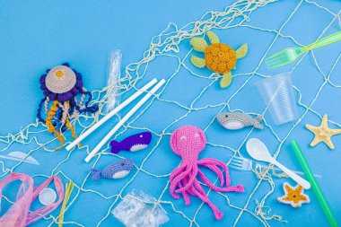 Dünya Okyanus Günü, su kirliliği farkındalığı ve çevresel eğitim görselleri. El yapımı tığ işi deniz hayvanları tek kullanımlık plastik eşyalar ve ağ, mavi arka plan, deri döşeme, üst görünüm