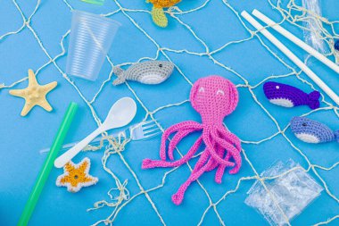 Dünya Okyanus Günü, su kirliliği farkındalığı ve çevresel eğitim görselleri. El yapımı tığ işi deniz hayvanları tek kullanımlık plastik eşyalar ve ağ, mavi arka plan, deri döşeme, üst görünüm
