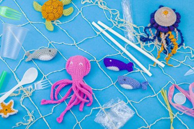 Dünya Okyanus Günü, su kirliliği farkındalığı ve çevresel eğitim görselleri. El yapımı tığ işi deniz hayvanları tek kullanımlık plastik eşyalar ve ağ, mavi arka plan, deri döşeme, üst görünüm