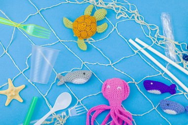 Dünya Okyanus Günü, su kirliliği farkındalığı ve çevresel eğitim görselleri. El yapımı tığ işi deniz hayvanları tek kullanımlık plastik eşyalar ve ağ, mavi arka plan, deri döşeme, üst görünüm