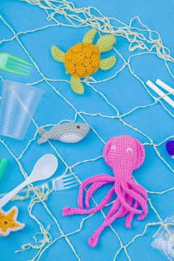 Dünya Okyanus Günü, su kirliliği farkındalığı ve çevresel eğitim görselleri. El yapımı tığ işi deniz hayvanları tek kullanımlık plastik eşyalar ve ağ, mavi arka plan, deri döşeme, üst görünüm
