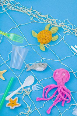 Dünya Okyanus Günü, su kirliliği farkındalığı ve çevresel eğitim görselleri. El yapımı tığ işi deniz hayvanları tek kullanımlık plastik eşyalar ve ağ, mavi arka plan, deri döşeme, üst görünüm