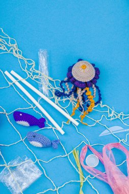 Dünya Okyanus Günü, su kirliliği farkındalığı ve çevresel eğitim görselleri. El yapımı tığ işi deniz hayvanları tek kullanımlık plastik eşyalar ve ağ, mavi arka plan, deri döşeme, üst görünüm