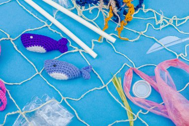 Dünya Okyanus Günü, su kirliliği farkındalığı ve çevresel eğitim görselleri. El yapımı tığ işi deniz hayvanları tek kullanımlık plastik eşyalar ve ağ, mavi arka plan, deri döşeme, üst görünüm