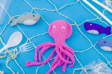 Dünya Okyanus Günü, su kirliliği farkındalığı ve çevresel eğitim görselleri. El yapımı tığ işi deniz hayvanları tek kullanımlık plastik eşyalar ve ağ, mavi arka plan, deri döşeme, üst görünüm