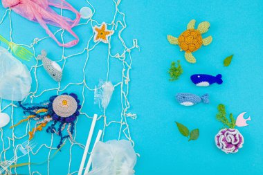 Dünya Okyanus Günü, su kirliliği farkındalığı ve çevresel eğitim görselleri. El yapımı tığ işi deniz hayvanları tek kullanımlık plastik eşyalar ve ağ, mavi arka plan, deri döşeme, üst görünüm